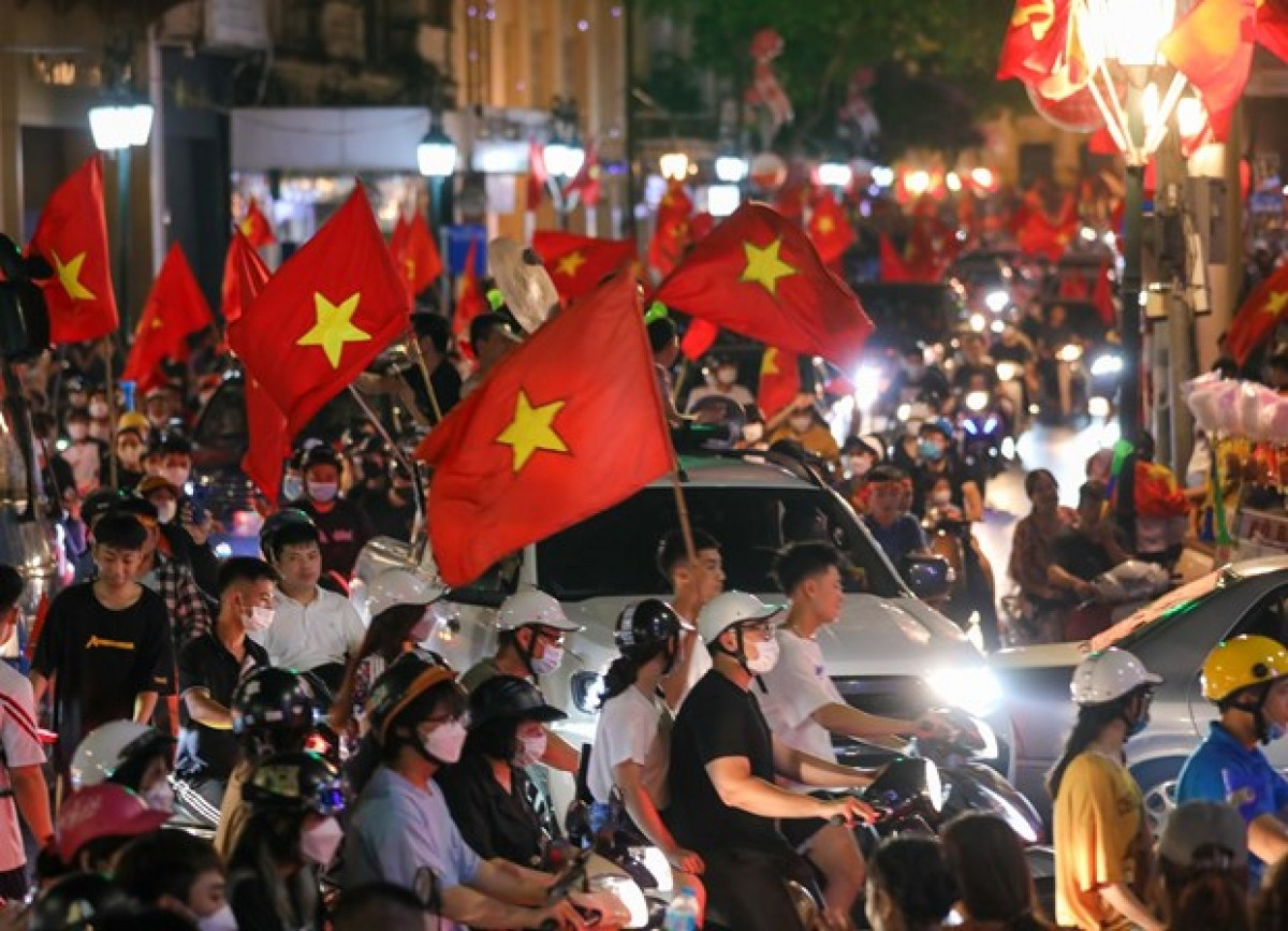 Thousands of people waving flags pour into the streets of Hanoi to celebrate the victory.