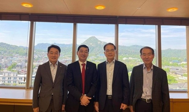 A group of men posing for a photo in front of a windowDescription automatically generated with medium confidence