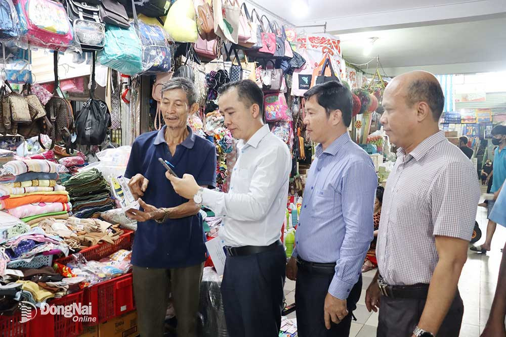 Tiểu thương Phạm Văn Phú (bìa trái) giới thiệu mã quét QR. Ảnh: N.Hà