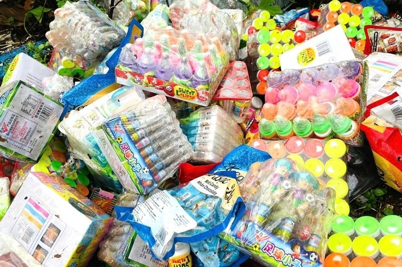 Hàng trăm gói kẹo đồ chơi trẻ em yêu thích đổ lộ thiên cạnh bãi rác
