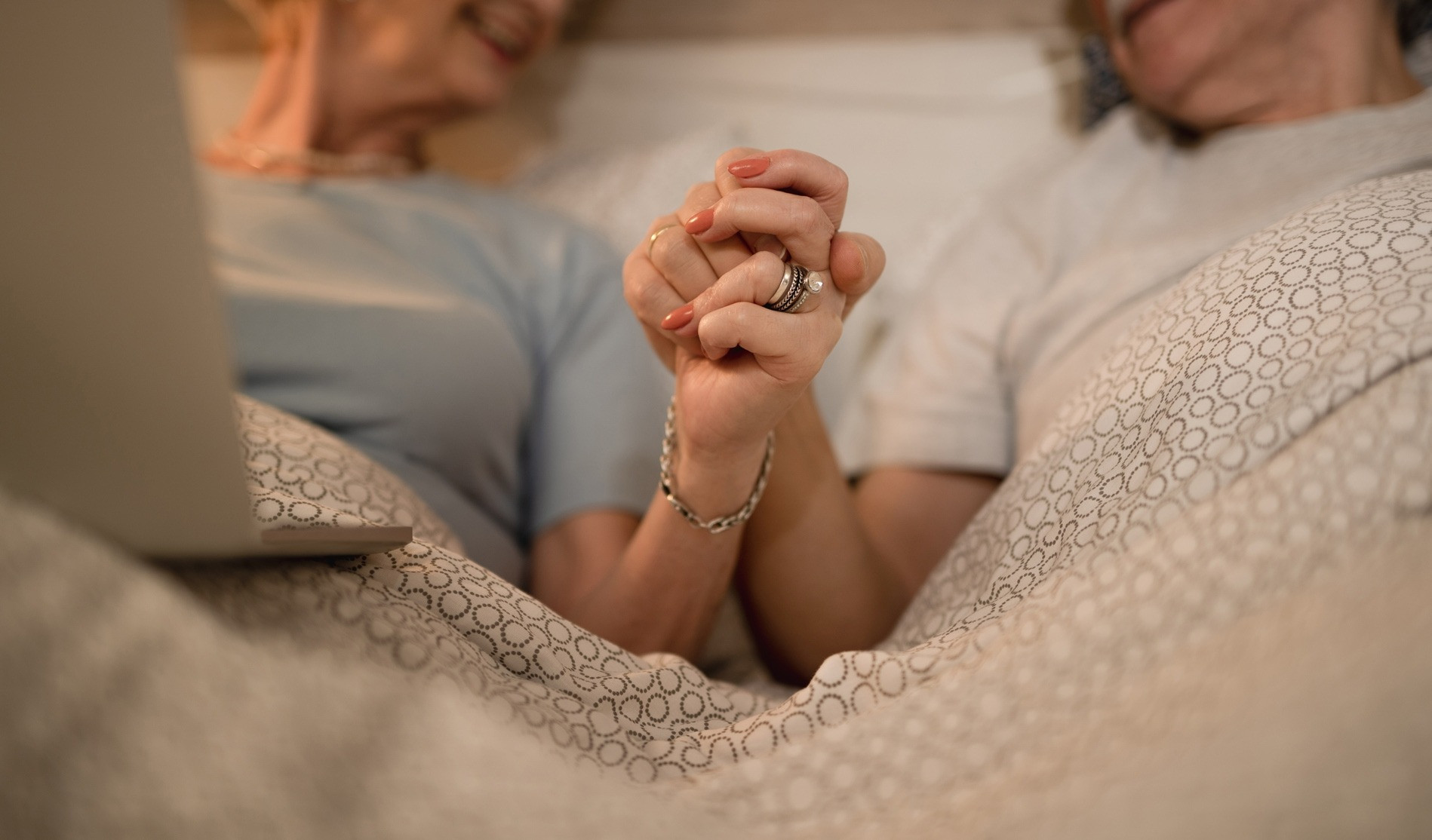 closeup affectionate senior couple holding hands while lying down bed evening.jpg