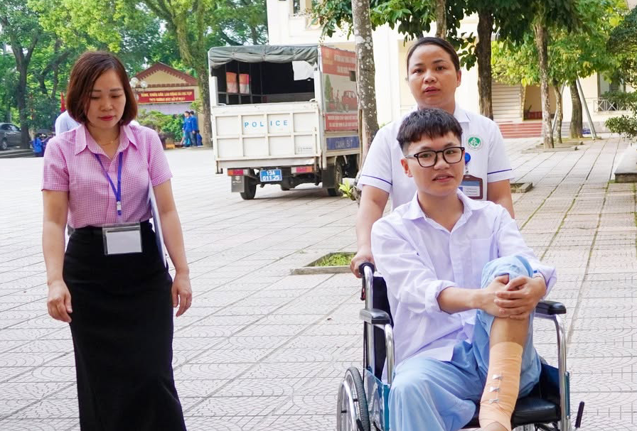Nhân viên y tế đẩy xe lăn đưa nam sinh đến phòng thi tốt nghiệp