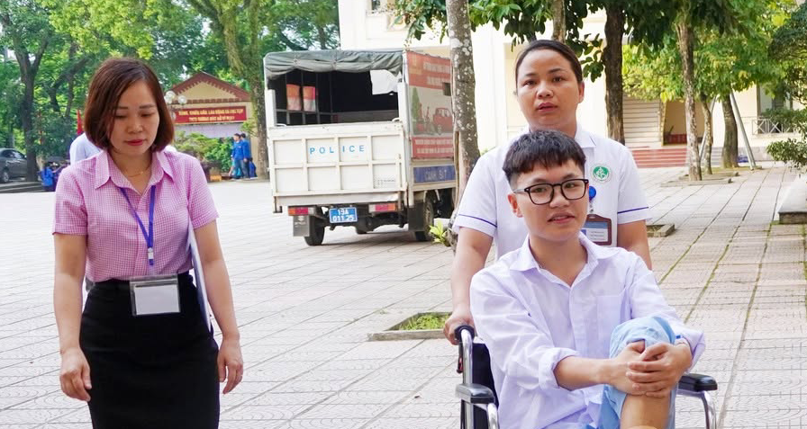 Nhân viên y tế đẩy xe lăn đưa nam sinh đến phòng thi tốt nghiệp