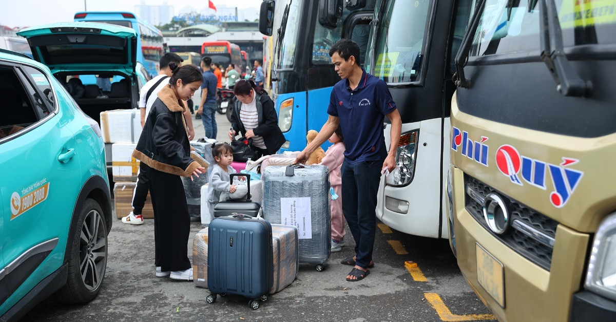 Passengers loading luggage beside intercity buses at a Vietnamese bus station.