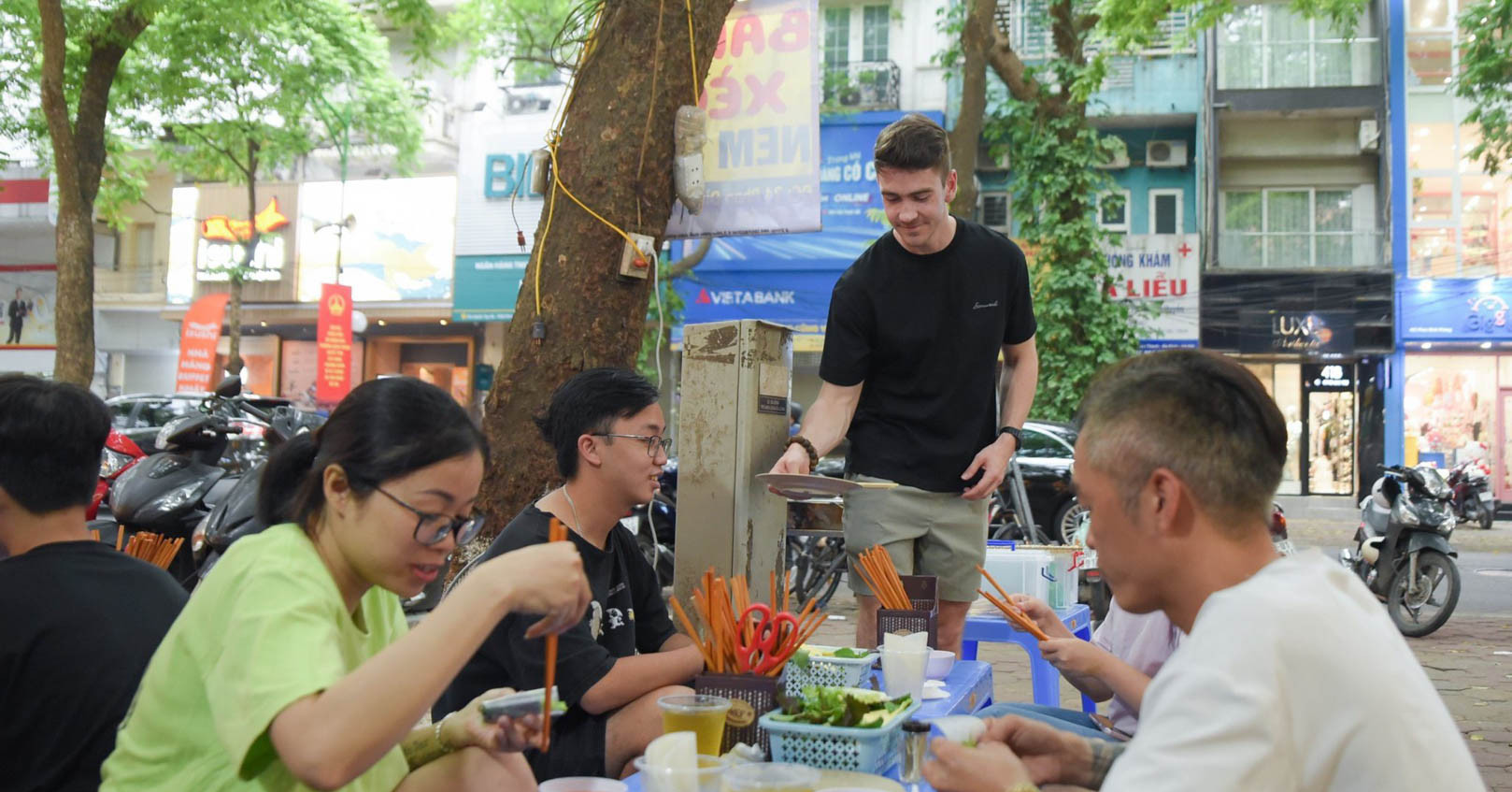 Foreign man grills nem lui, sells banh xeo at pavement shop in Hanoi